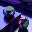 Two M3 Mini Colorful Wireless Speakers by Dropshipman, featuring metallic spherical designs and reflective surfaces, rest on a glossy surface illuminated by blue and purple lights.