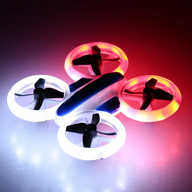 The Dropshipman RC Quadcopter Drone S123, a compact drone with altitude hold, 6-axis gyro, and two white LED-lit propellers plus two red LED-lit propellers, sits on a smooth surface with its lights reflecting below.