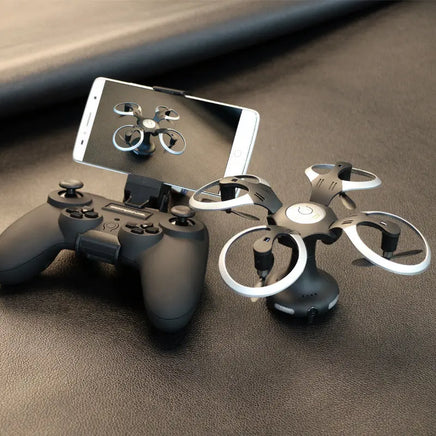 The Dropshipman High-definition Aerial Photography of Drones, in black and silver, sits with its controller and a smartphone streaming a live HD feed—creating a sleek, portable setup on a dark textured surface.