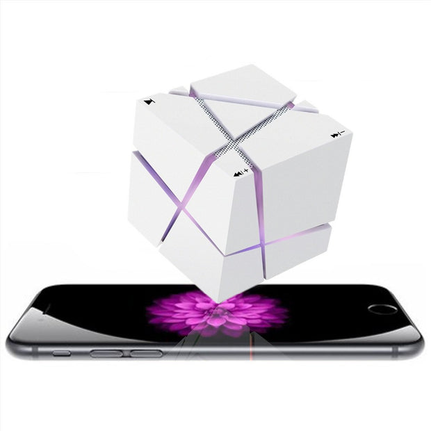 The Dropshipman CubeSync Rubik Cube Bluetooth Speaker with glowing purple lines floats above a smartphone displaying a pink flower against a white background.
