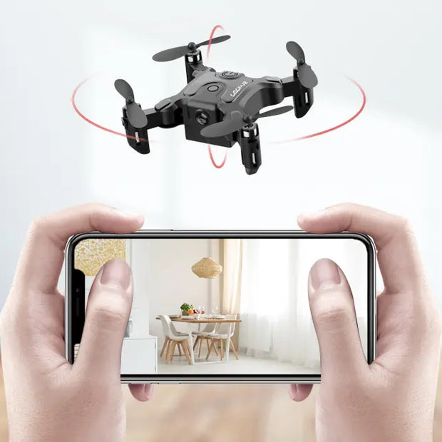 A person holds a smartphone showing a bright dining room, while the Dropshipman Mini folding drone with red indicator lights hovers indoors, highlighting its remote control quadcopter features.