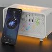 A smartphone leans against the Dropshipman 3 In 1 Bluetooth Speaker White Noise Speaker, which features glowing lights and colorful musical notes, resting on a dark surface.