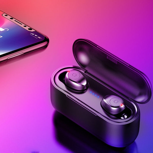 A pair of Dropshipman F9 wireless headphones with charging case sits open next to a smartphone on a purple and pink gradient surface, glowing with indicator lights like an Avengers LED Face Mask.