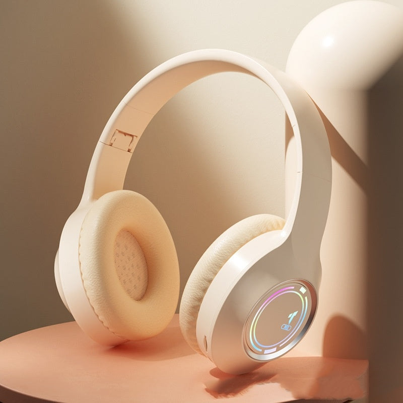 The Dropshipman M3 Light-emitting Headphones feature soft beige ear cushions and a colorful circular LED display showing battery status, emphasizing their long battery life. Shown resting on a peach surface under warm, gentle lighting.