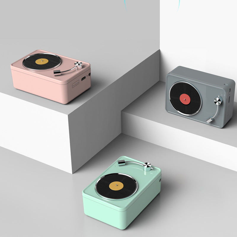 Three Dropshipman Retro Vinyl Record Wireless Speakers in pastel pink, gray, and mint green sit on minimalist white platforms at different heights, creating a stylish display against a light background.