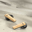 Two wooden push-up bars with black round bases rest on a textured beige surface among scattered stones—creating a stylish workout vibe that pairs perfectly with your Dropshipman Wood Grain Wireless Bluetooth Earbuds.