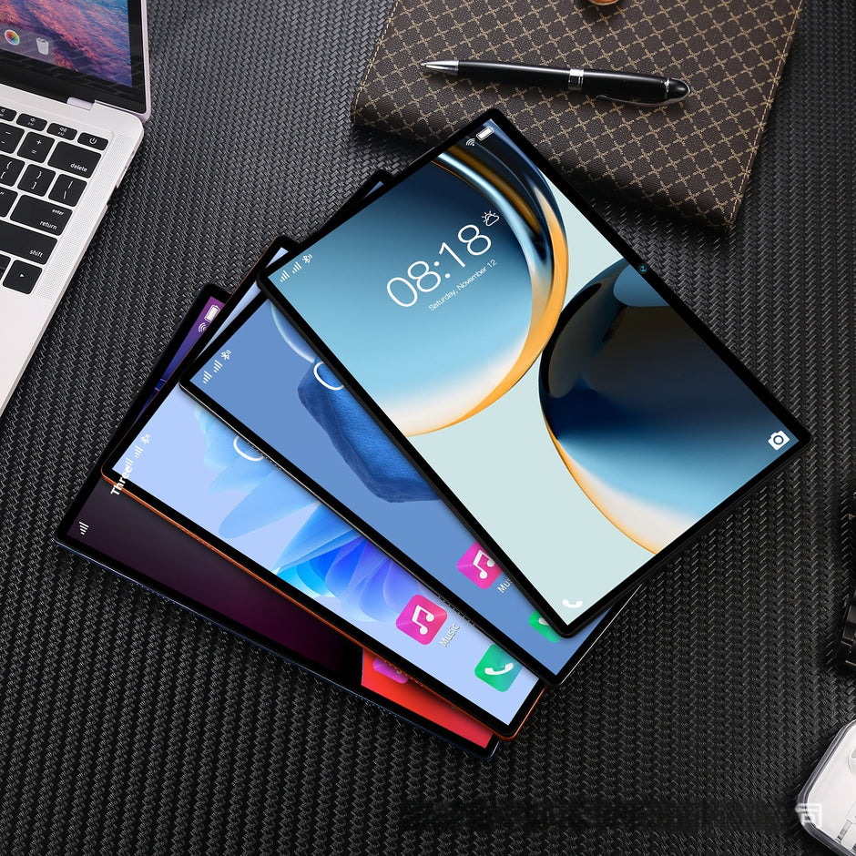 Three Dropshipman Home Tablet and Gaming Computers overlap on a textured black surface near a laptop, patterned notebook, pen, and a 10.1-inch detachable keyboard tablet.