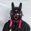 A person wearing HeadphoneHeat's futuristic LED Lights Cyberpunk Full Face Mask features rabbit-ear-like details and vivid LEDs illuminating their matching black outfit. Bright pink ribbons hang from the sides, set against a plain white fabric backdrop.