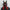 A person wears a HeadphoneHeat LED Lights Cyberpunk Full Face Mask that resembles a futuristic sci-fi helmet. Primarily black with red accents, it has tall, pointed extensions and LEDs for an eerie glow. Paired with a dark cloak, this ensemble exudes enigmatic allure.