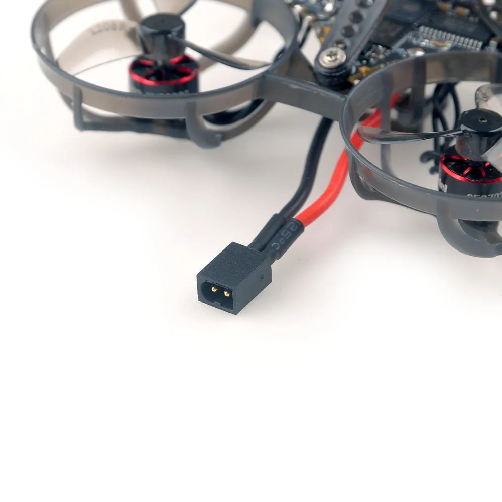 A close-up of the HappyModel Mobula6 2024 1S 65mm Ultra Light Micro FPV Drone2 by HeadphoneHeat shows its exposed wiring and two visible propellers. It features a SuperX Flight Controller, with a red and black power cable extending out and ending in a black two-pin connector, all set against a simple white background.