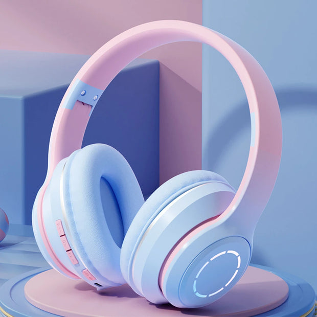 The pastel pink and blue Wireless HiMISS HiFi Stereo Over Ear Headphones by HeadphoneHeat rest on a blue surface. They feature cushioned ear pads and possible side control buttons. The background has matching geometric shapes, enhancing their stylish appeal and Bluetooth-like design.