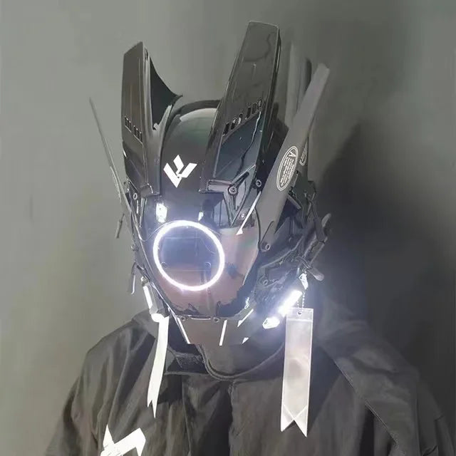 The LED Lights Cyberpunk Full Face Mask by HeadphoneHeat features an angular, robotic design with a glowing central light. Its sci-fi aesthetic is enhanced by geometric shapes and metallic elements, set against a plain background.