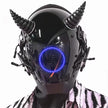 Wearing the HeadphoneHeat LED Lights Cyberpunk Full Face Mask, a sleek black helmet with conical horns and a glowing circle on the faceplate, paired with side mechanical details, perfectly complements a patterned garment for a modern vibe.
