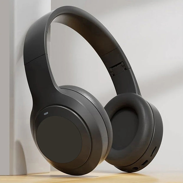 The HeadphoneHeat V5.3 Over-Ear Headphones in sleek black rest upright on a wooden surface, showcasing plush ear cup padding and a minimalistic design for high-quality audio and a lightweight fit.