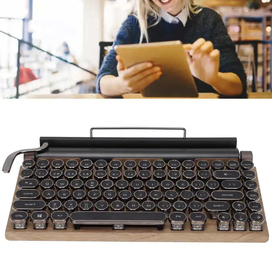 A person is smiling while using a tablet in the background. In the foreground, there's a HeadphoneHeat Retro Typewriter Mechanical Keyboard with round keys, wooden base, and Bluetooth 5.0 connectivity, resembling a classic typewriter.
