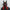 A person in black attire wears a futuristic HeadphoneHeat LED Lights Cyberpunk Full Face Mask. It features red and black accents, angular antenna-like extensions, a reflective visor, intricate side details, and LED lights on top for a sleek robotic look.