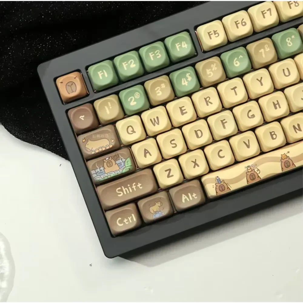 The HeadphoneHeat Capi Bara Mechanical Keyboard boasts whimsical keycaps with nature and building illustrations in green, brown, and beige. Each uniquely designed key ensures comfort with its ergonomic design on a sleek black-and-white surface, complete with wireless technology.