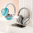 Two pairs of HeadphoneHeat's Bluetooth HIFI Headphones Wireless Stereo, one in blue and the other in gray, are displayed on a white surface next to a smartphone. Enjoy wireless freedom in a minimalist setting with soft lighting.
