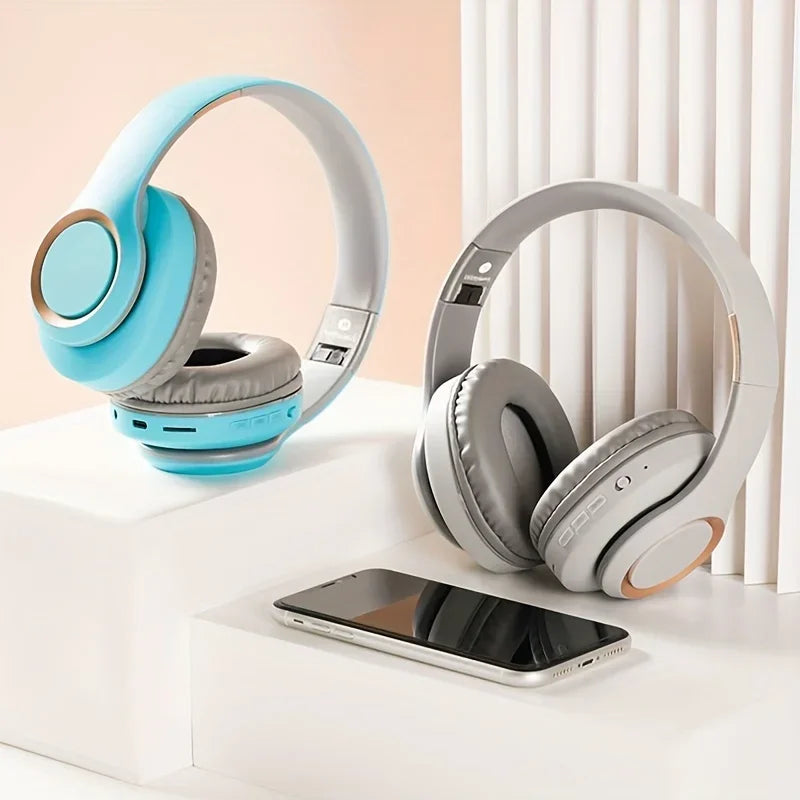 Two pairs of HeadphoneHeat's Bluetooth HIFI Headphones Wireless Stereo, one in blue and the other in gray, are displayed on a white surface next to a smartphone. Enjoy wireless freedom in a minimalist setting with soft lighting.