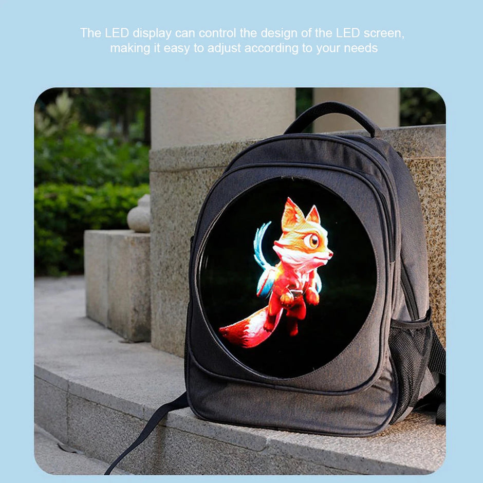 A BSIDE 3D Holographic Projector Backpack by HeadphoneHeat sits on a stone ledge outdoors. The front of the backpack features an LED screen displaying an animated fox. Above the backpack, text reads, "The high-resolution LED display can control the design of the screen, making it easy to adjust according to your needs.