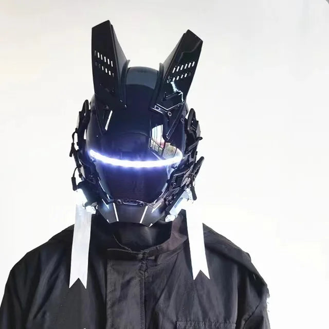 Wearing the HeadphoneHeat LED Lights Cyberpunk Full Face Mask, a person dons a futuristic helmet featuring rabbit ear-like extensions and a bright visor. This intricately detailed black mask with subtle LED lights complements their dark outfit against a plain white background.