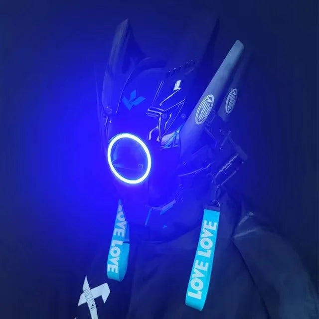 Wearing the LED Lights Cyberpunk Full Face Mask from HeadphoneHeat, a person sports a sleek black helmet with glowing blue elements and "LOVE" text on blue straps. It exudes a futuristic, robotic design against a dark blue backdrop.