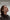 A person with shoulder-length brown hair is wearing a dark button-up shirt and the AI Earphone Translator Erazer XP6 Bluetooth Earphones from HeadphoneHeat. They appear relaxed, with eyes closed, against a neutral background. Text above reads: 