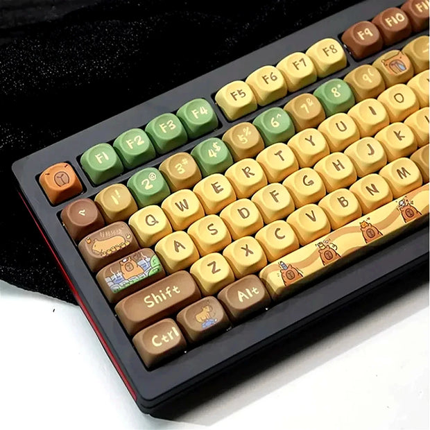 Introducing the Capi BaraCapi Bara Mechanical Key Keyboard by HeadphoneHeat—a wireless mechanical keyboard featuring ergonomically designed round keycaps in green, yellow, and brown hues. Each keycap displays unique retro-style icons such as a house and a tree, while the entire keyboard rests elegantly on a sleek black surface.