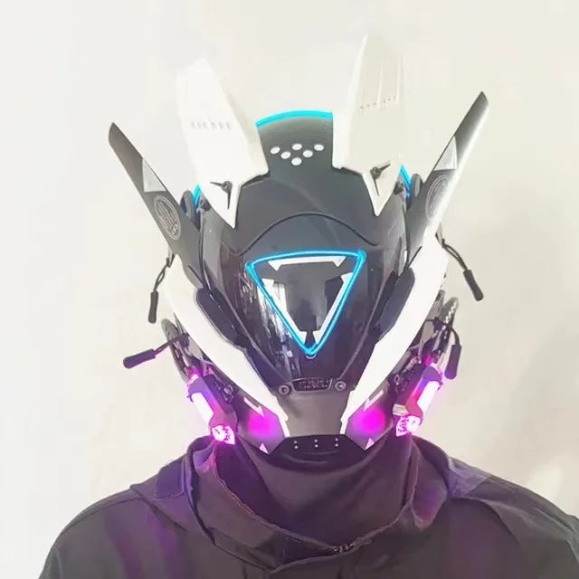 A person wears the HeadphoneHeat LED Lights Cyberpunk Full Face Mask, which showcases glowing blue and pink LEDs, sharp white and black details, and a triangular front design. The mask covers the entire head and is complemented by a dark outfit.