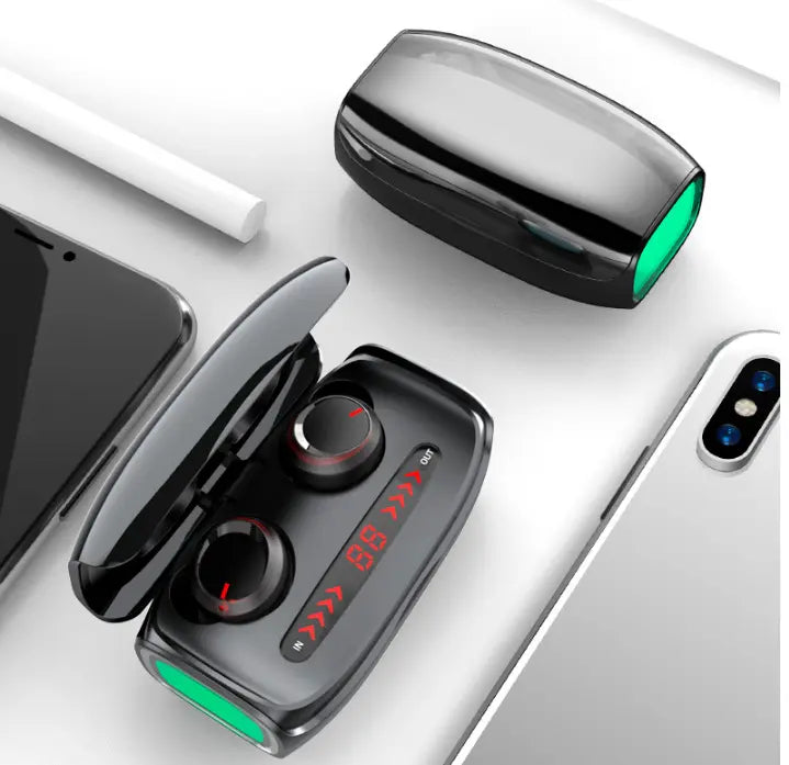 A pair of FLIPSTYLEZLLC T11 Wireless Bluetooth Headset 5.0 Earbuds in an open charging case with LED display rests on a white surface beside a smartphone, tablet, and another closed case.
