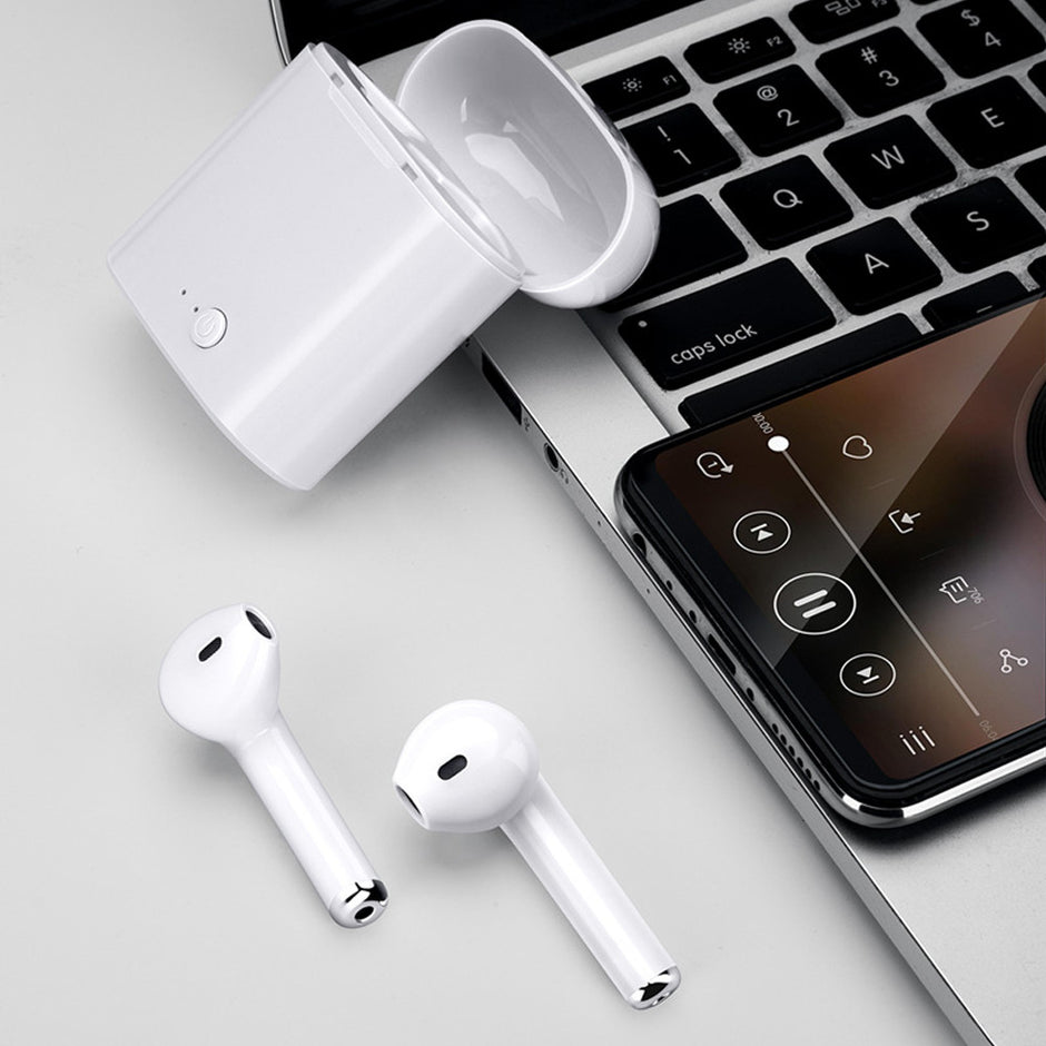A pair of white Dropshipman Universal Earbuds with charging case sit on a laptop keyboard beside a smartphone with a music app, delivering immersive audio for your daily soundtrack.
