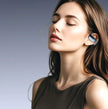 A young woman with long brown hair, eyes closed and looking relaxed, wears Dropshipman YYK-Q17 Noise-canceling Bluetooth Earbuds against a blue-grey background, enjoying their extra-long battery life.